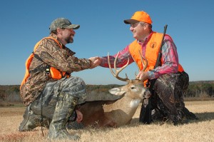 Two man hunters shaking hands over a dead deer.