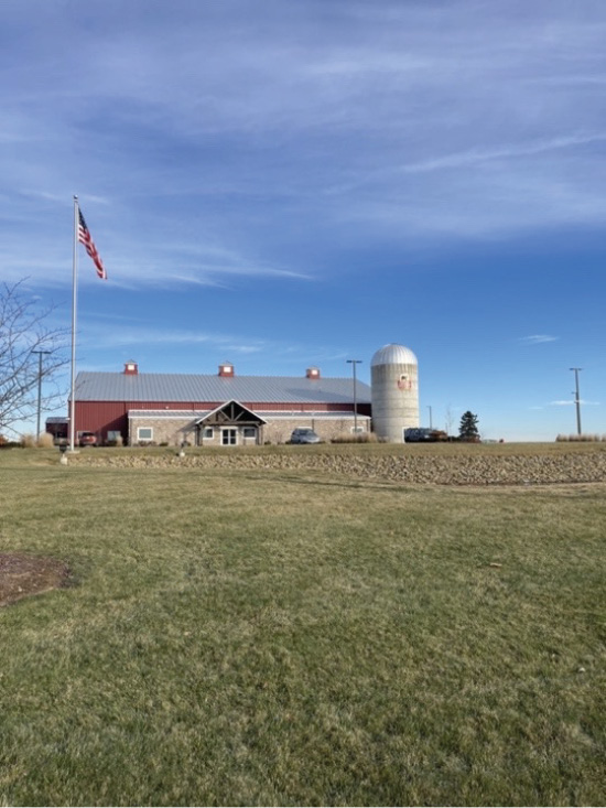 Green grass beneath a big red house and a blue sky