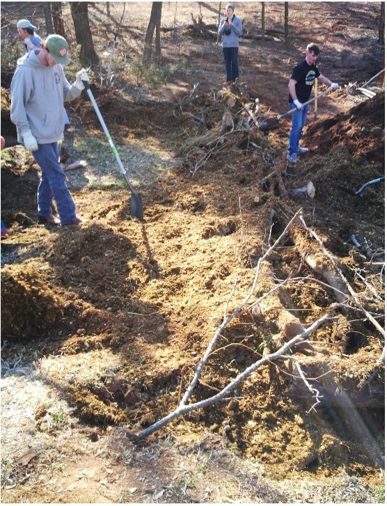 Figure 12 Sustainable Landscapes HLA-6478 A group of 4 people covering logs and branches with mulch or compost to fill gaps and add nitrogen for decomposition in a hügelkultur bed.