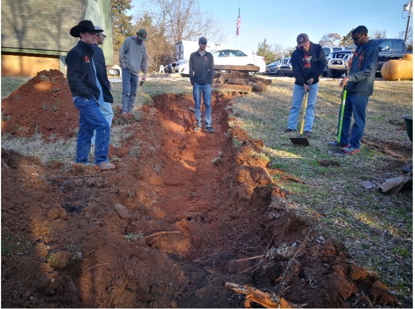 Figure 9 Sustainable Landscapes HLA-6478 A group of 5 people working in a grassy area digging a long curved trench with shovels and tools.