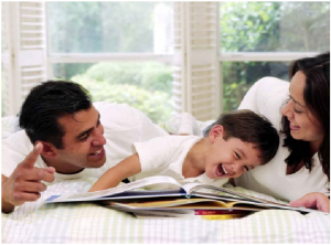 A man, woman and child laying on a bed laughing and reading a book.