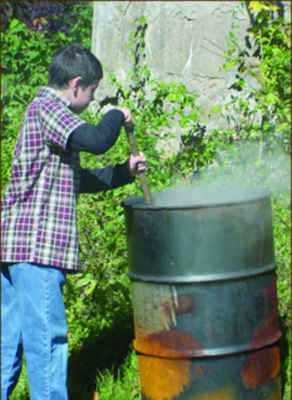 A teenager burning trash in a burn barrel