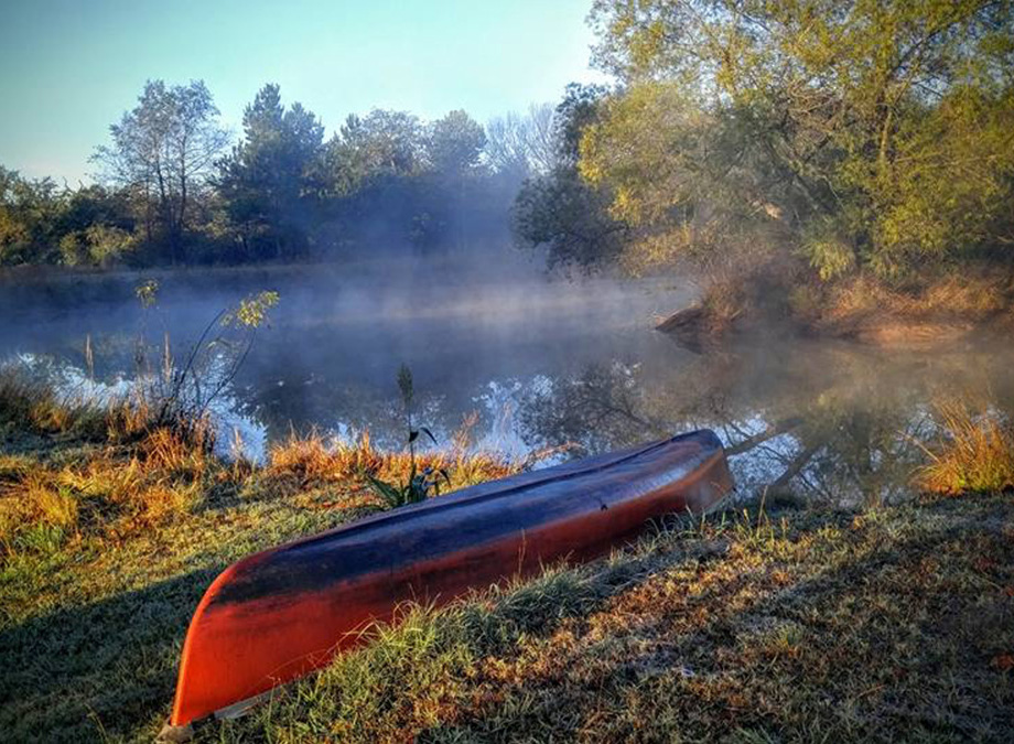Red canoe turned upside down in the grass in front of a misty pond. Red canoe turned upside down in the grass in front of a misty pond.