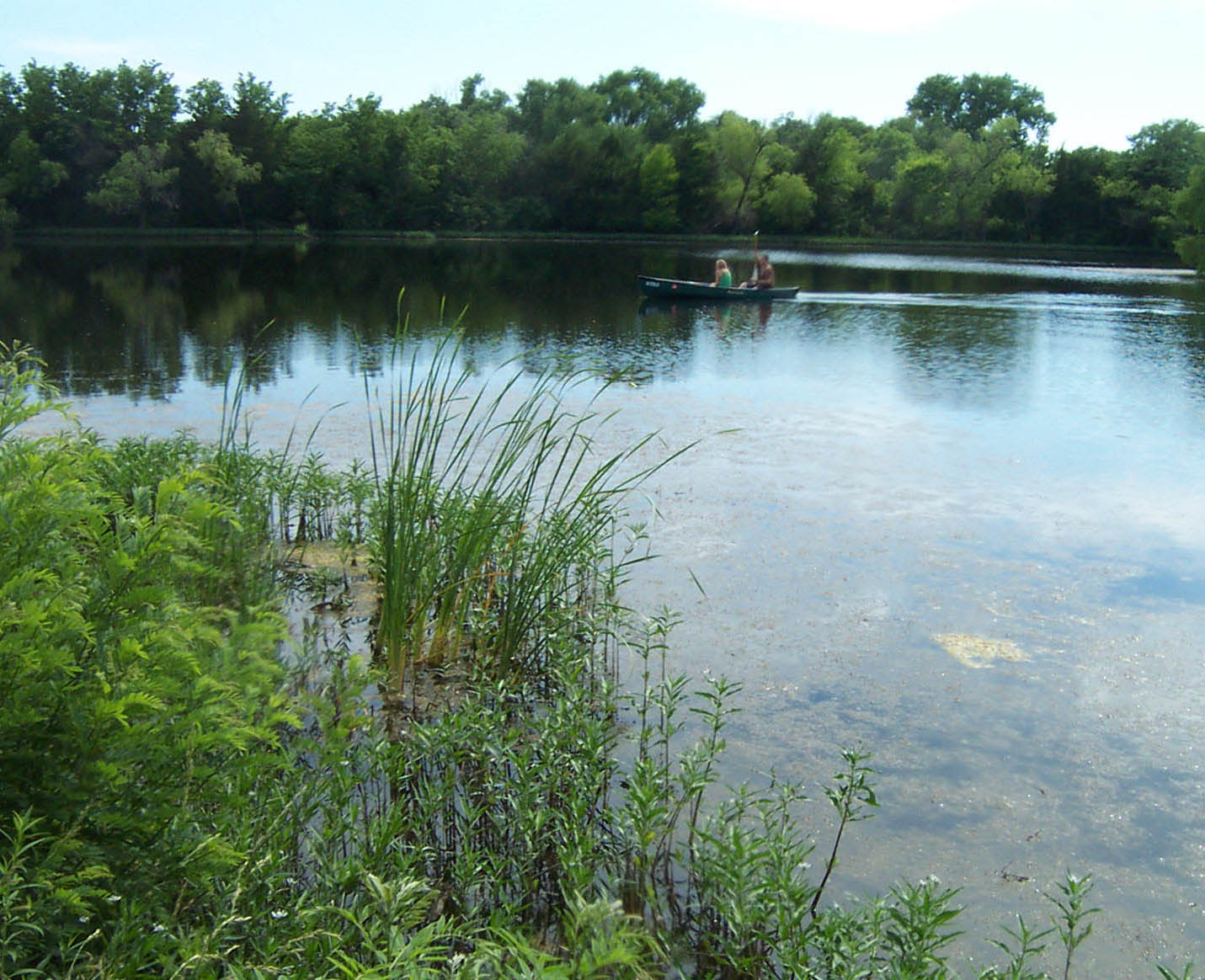 A pond with two men on a sall boat fishing in the middle of it. A pond with two men on a sall boat fishing in the middle of it.