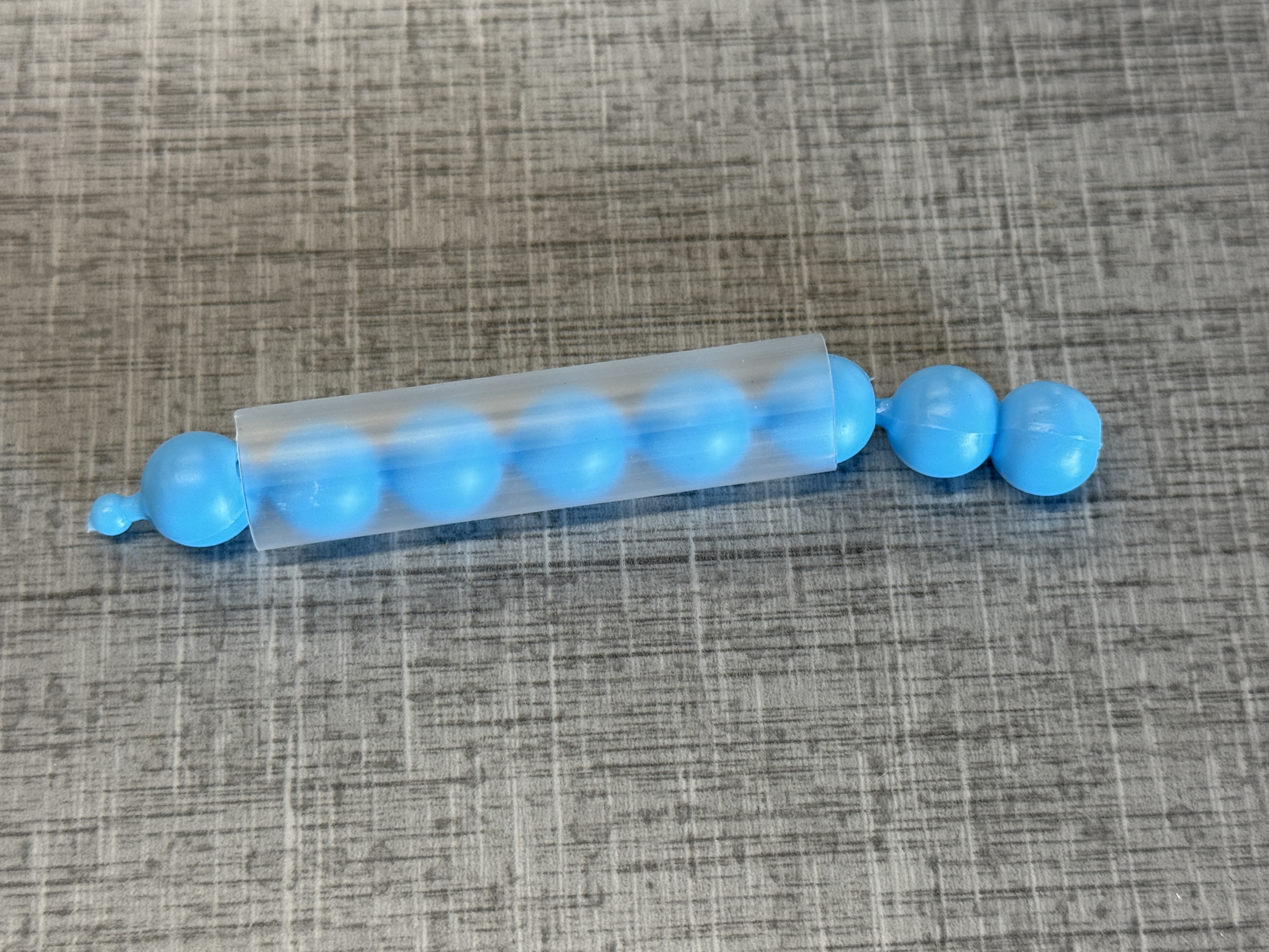 Blue pop beads in a clear plastic straw.