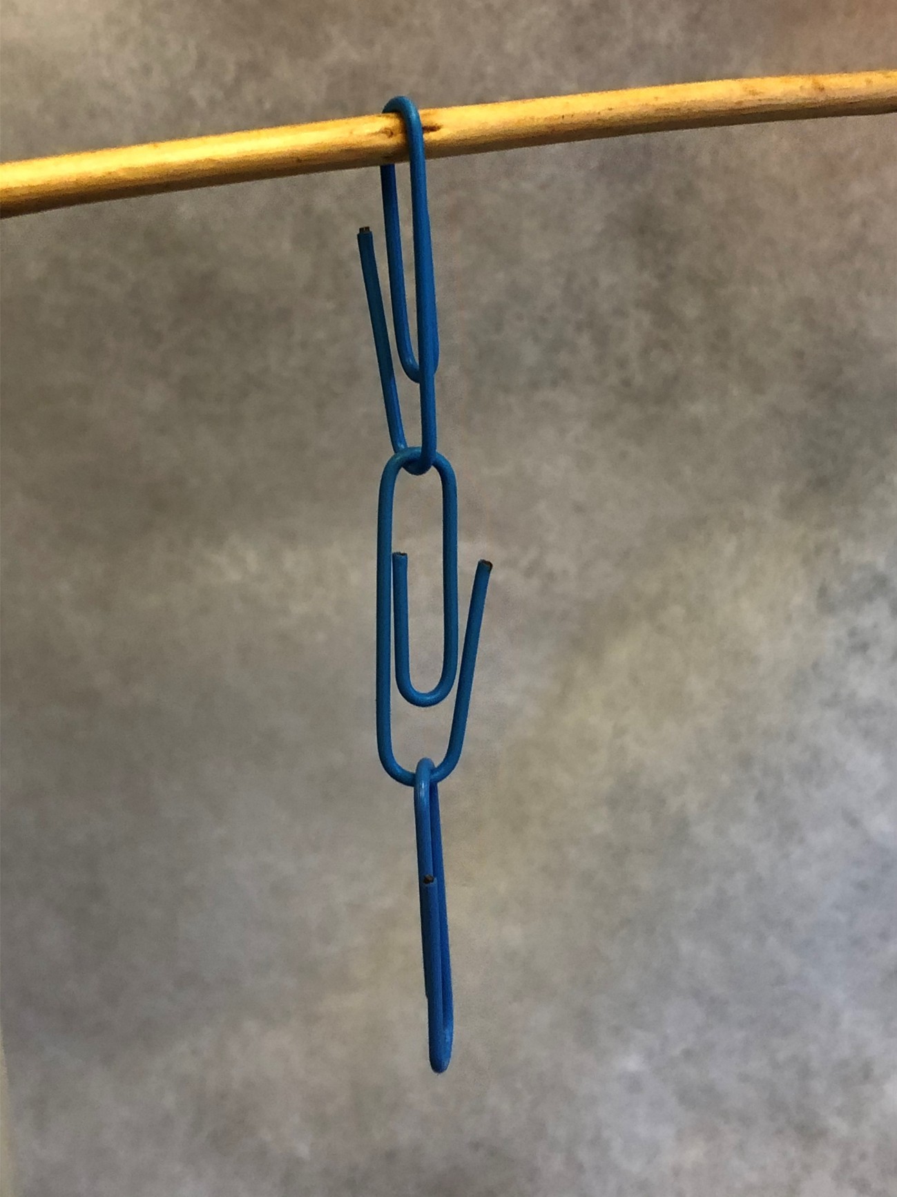 Three blue paper clips hanging from a wire.
