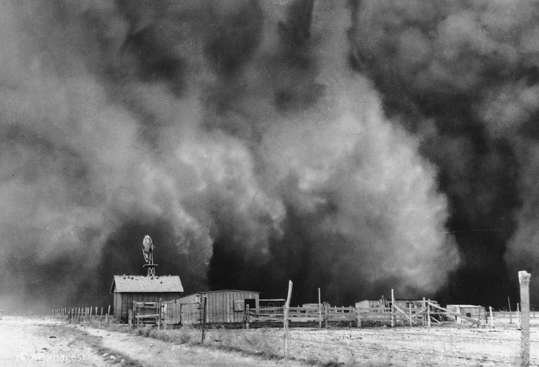 A black and white photograph from the 1930s showing a dust storm on farmland.