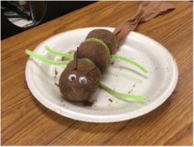 A white plate sitting on a table that has three brown balls of soil in the shape of a caterpillar with googly eyes.