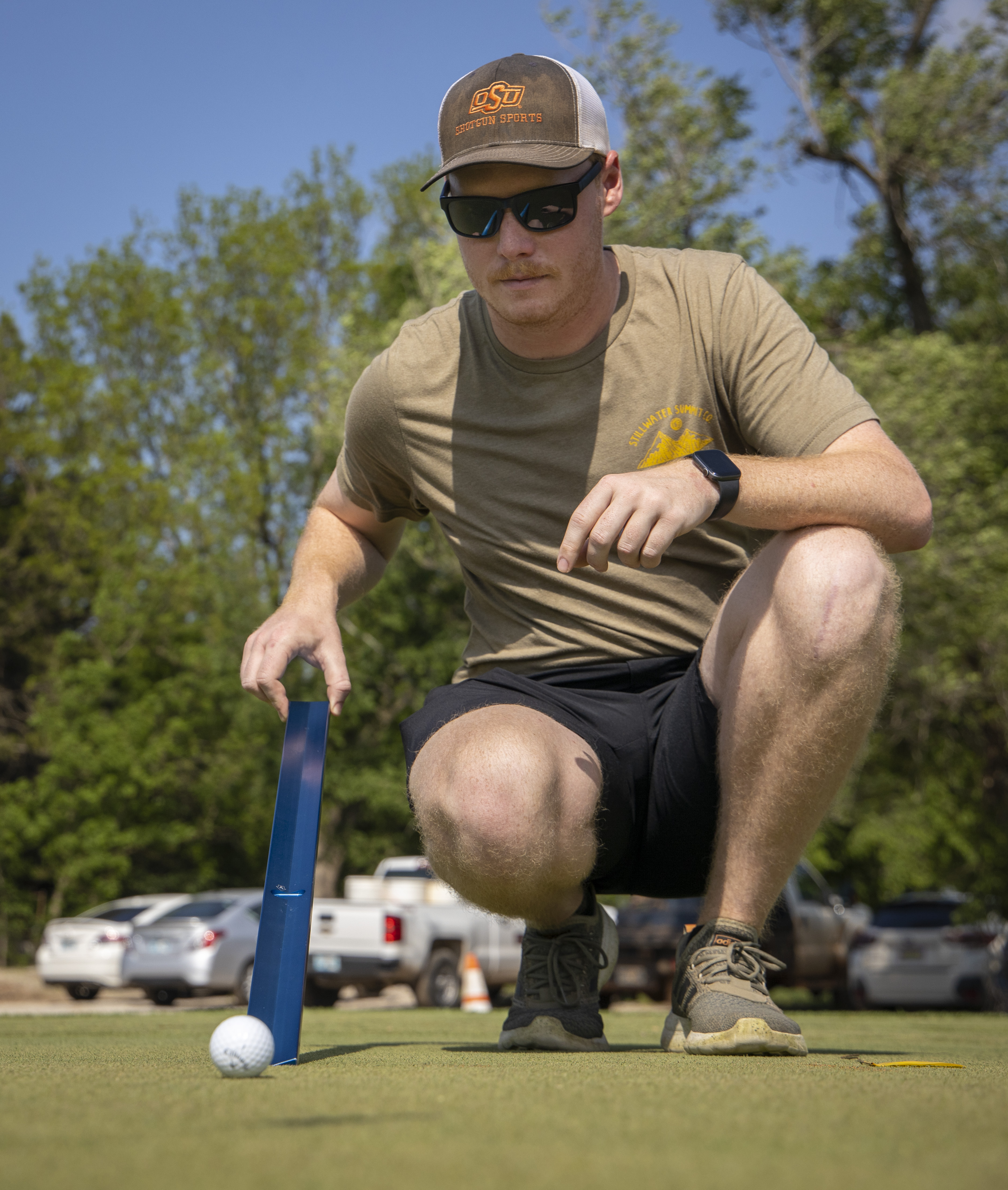 A person using a blue stimpmeter to measure the distance that the gold ball rolled.