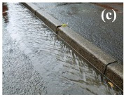 Rainwater flowing along a concrete curb into a street gutter.