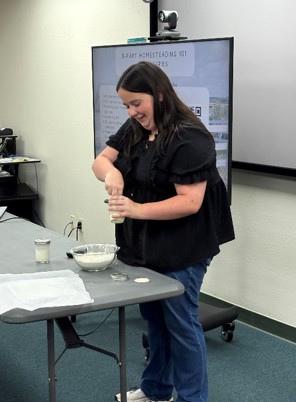A girl in a black shirt standing at the front of the classroom as she demonstrates on how to make homemade biscuits.