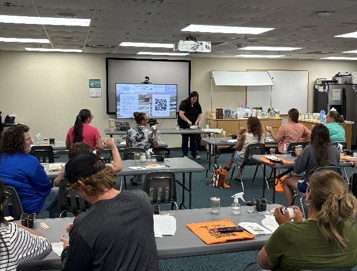 Participants sitting in rows of tables inside of a classroom as they work on making their own butter.