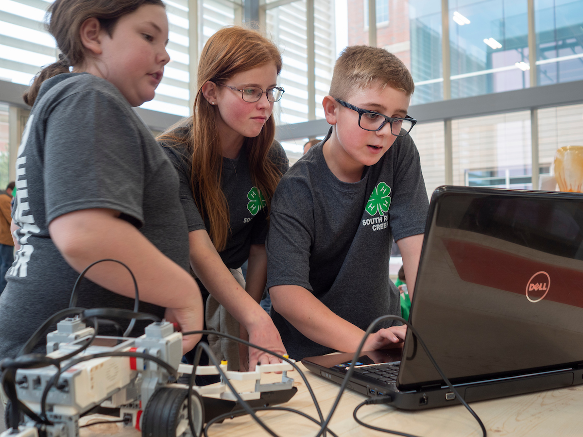 Three youths standing around a laptop collaborating for a robotics competition.