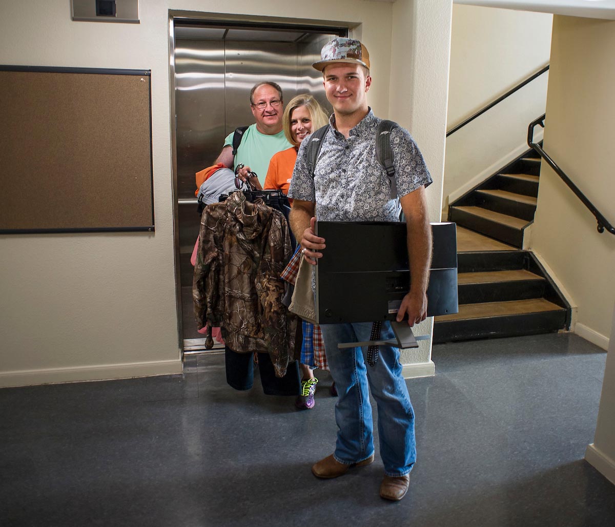 Parents helping their son move into the dorms. Stood oustide an elevator.
