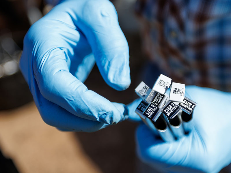 Two hands in rubber gloves holding test tubs.