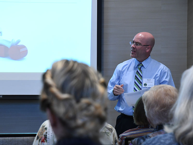 A man next to a projector screen talking to a crowd of people.