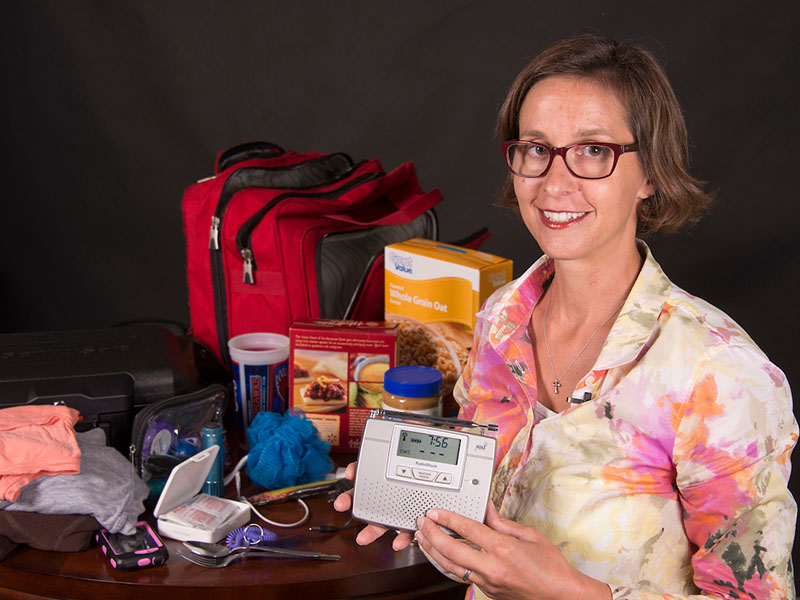 A woman standing in front the contents of a disaster survival kit.