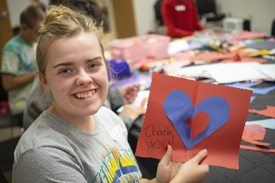 A girl holding up a red piece of paper with a blue heart drawn on it that says "thank you"..