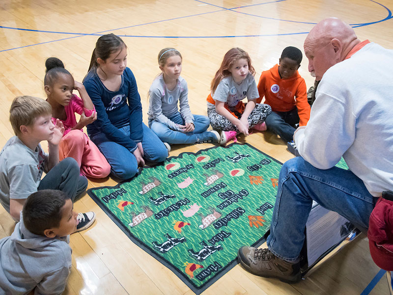 A man sitting in a chair presenting to a group of children.