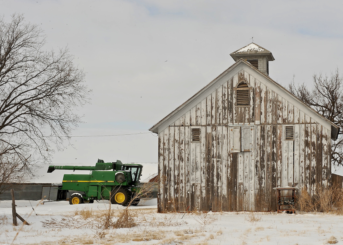 Wooden barn and tractor on snow covered ground.