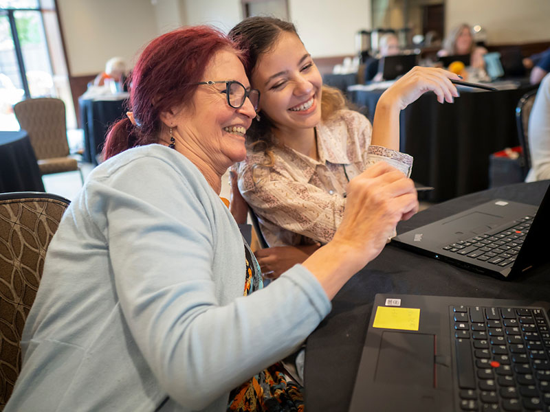 Two women setting with their computer laughing.