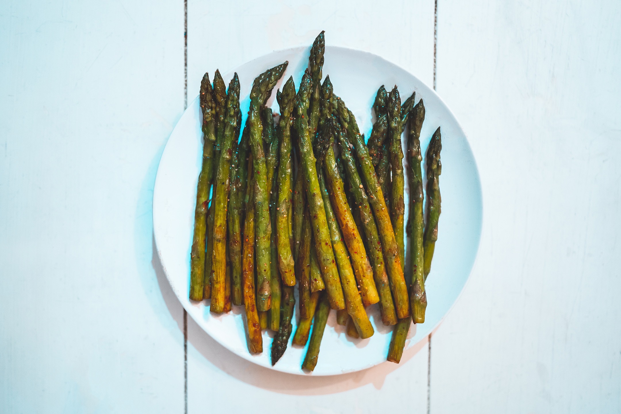 Cooked asparagus on a white plate sitting on a table.