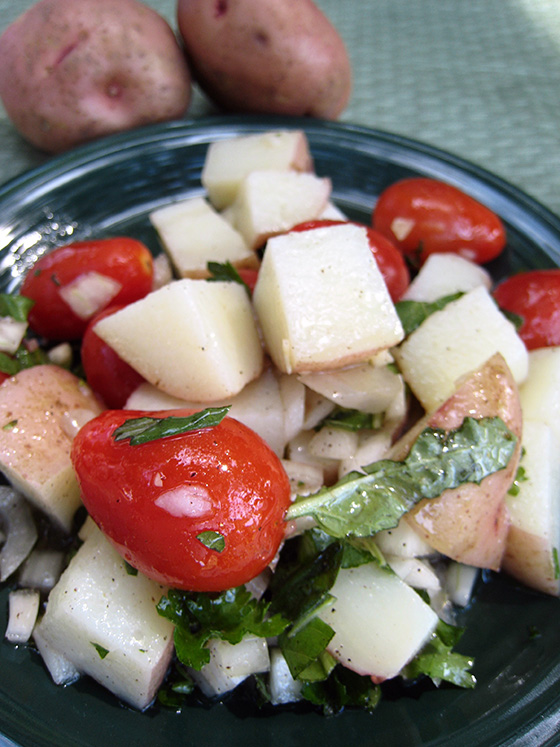 Basil potato tomato salad on a plate with potatoes in the background.