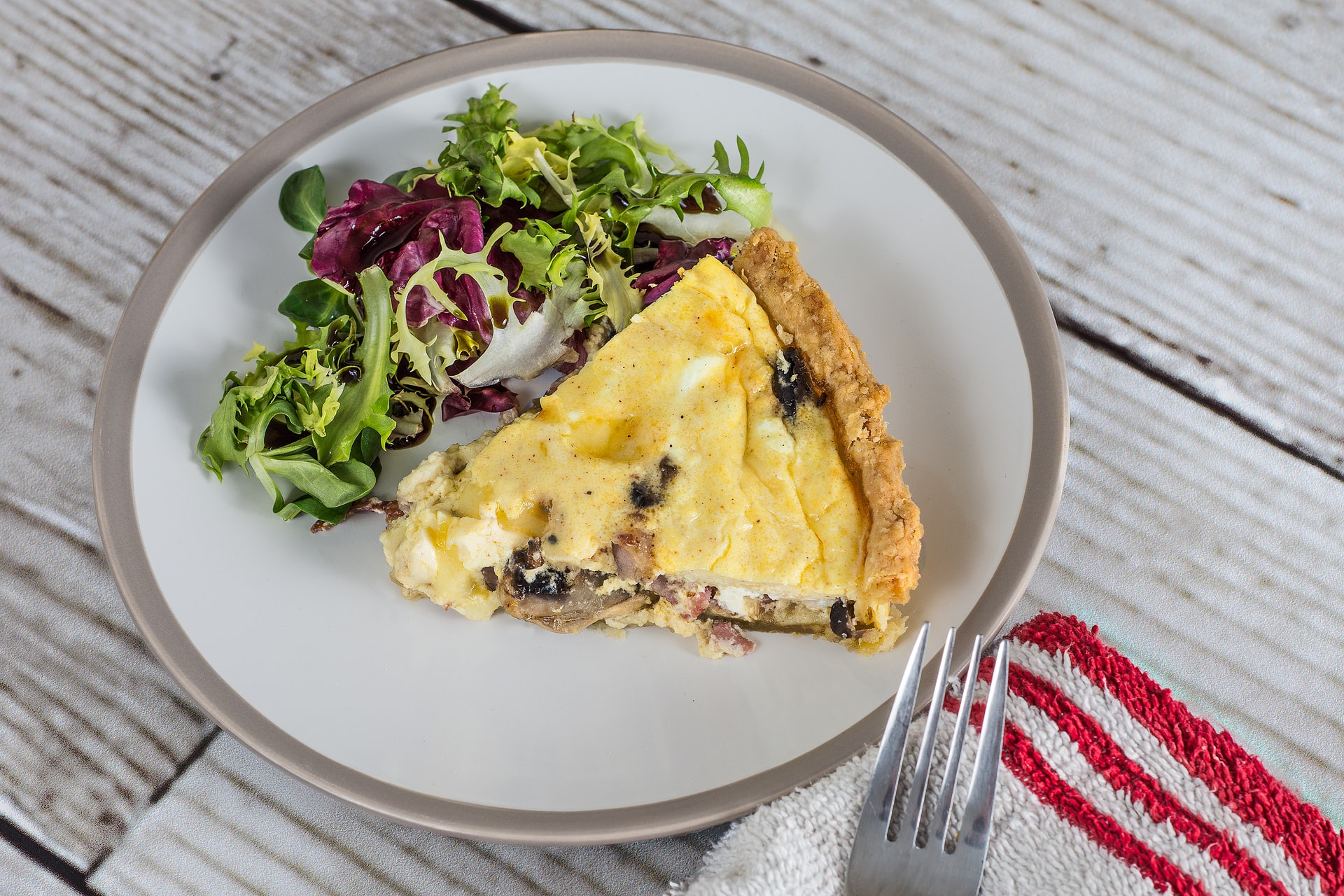 A quiche with mushrooms on a plate with a salad on the side.