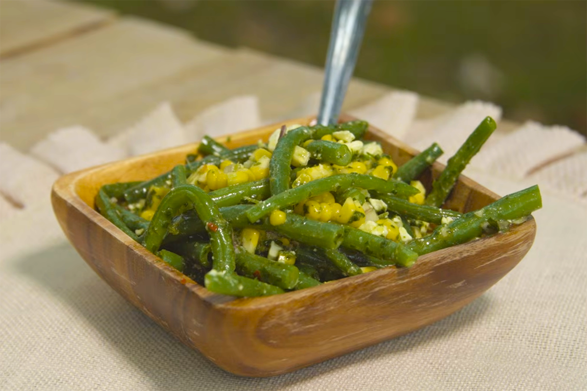 A wooden bowl of fresh green bean salad served with a fork.