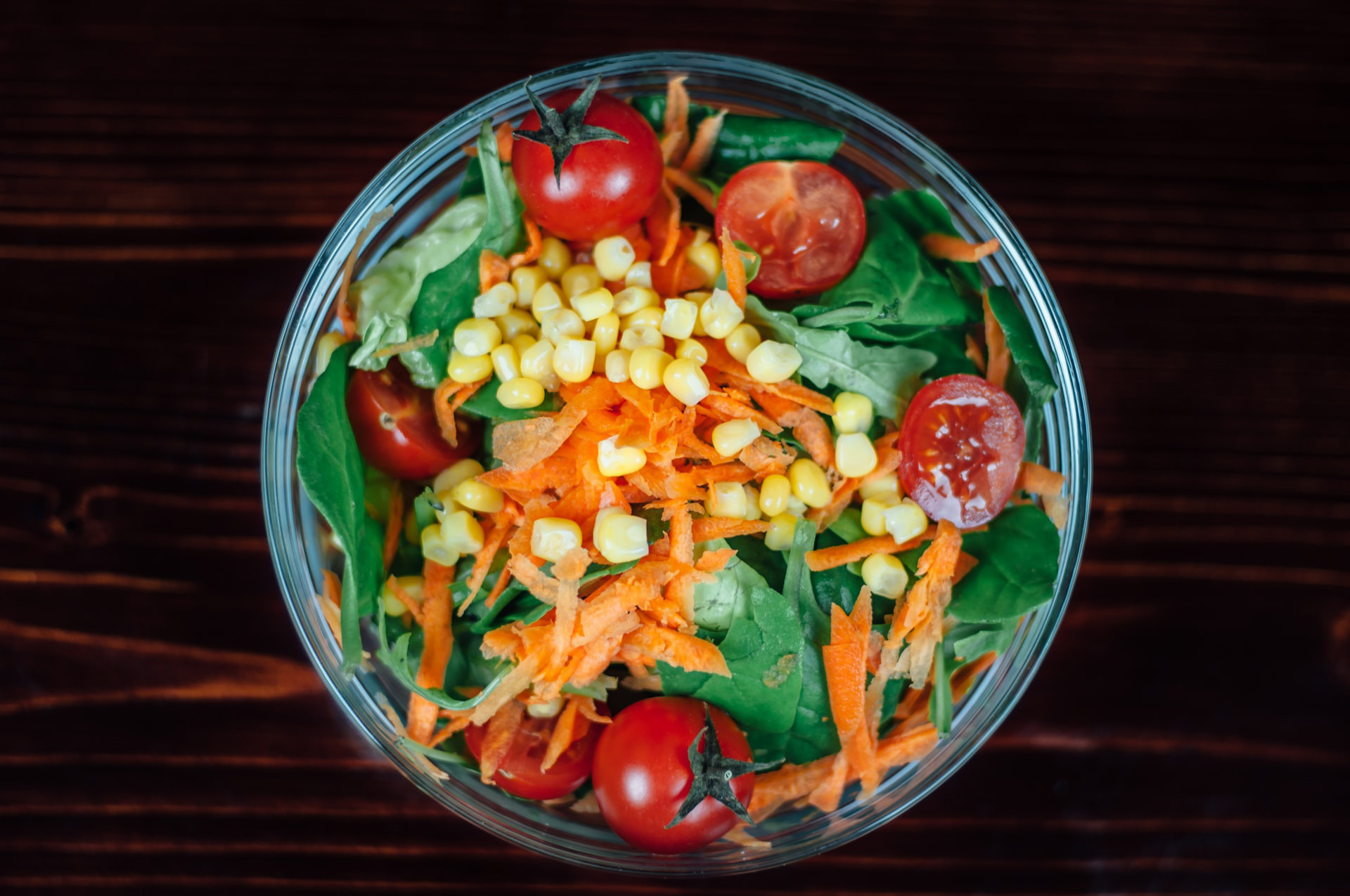 A corn salad in a bowl with greens, tomatoes and shredded carrots.