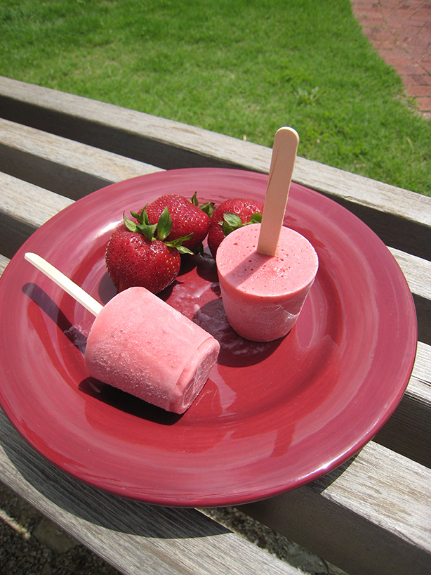Frozen strawberry pops on a plate with fresh strawberries on the side. 