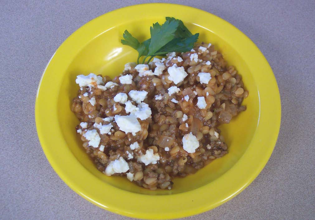 A greek skillet recipe in a yellow bowl with feta cheese on top.