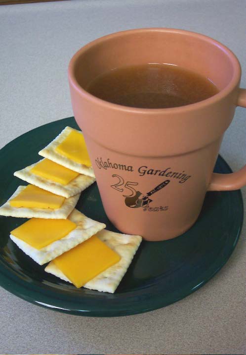 A brown mug full of tea on a green plate with crackers and cheese. 