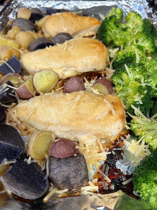Chicken breast with potatoes and broccoli topped with parmesan cheese on a sheet pan.