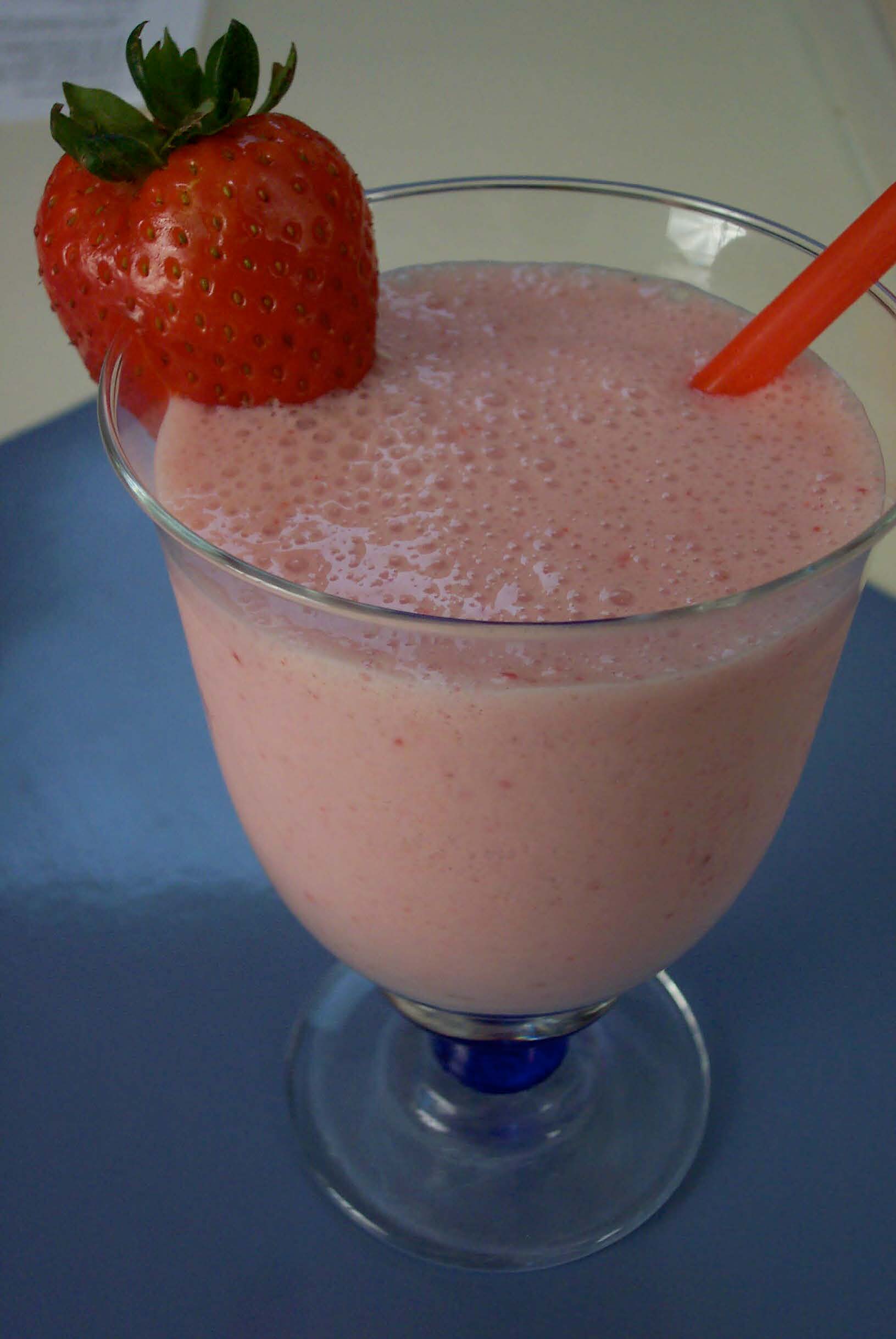 A pink looking smoothie in a clear glass with a strawberry on the rim.