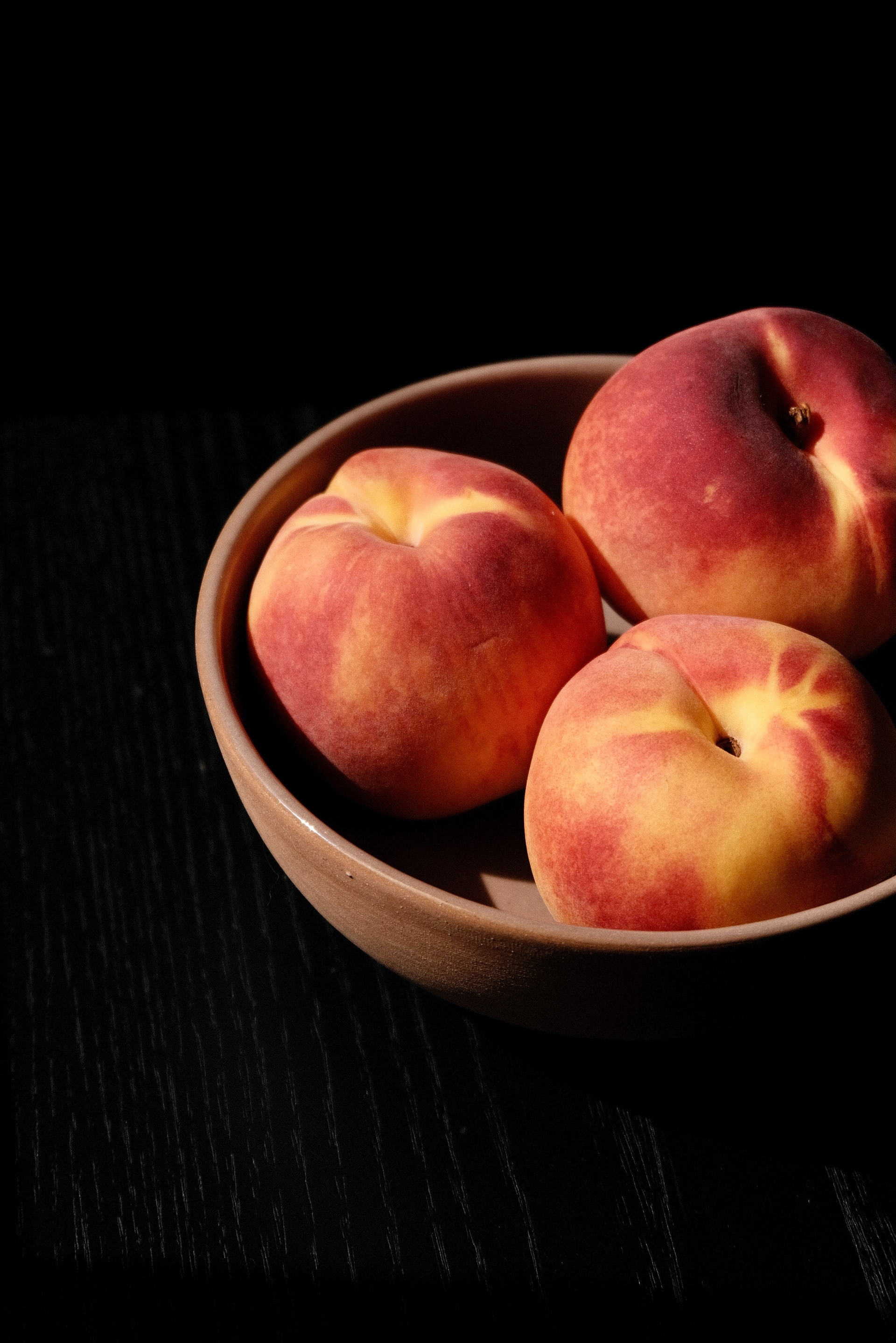 A brown bowl with three peaches in it.