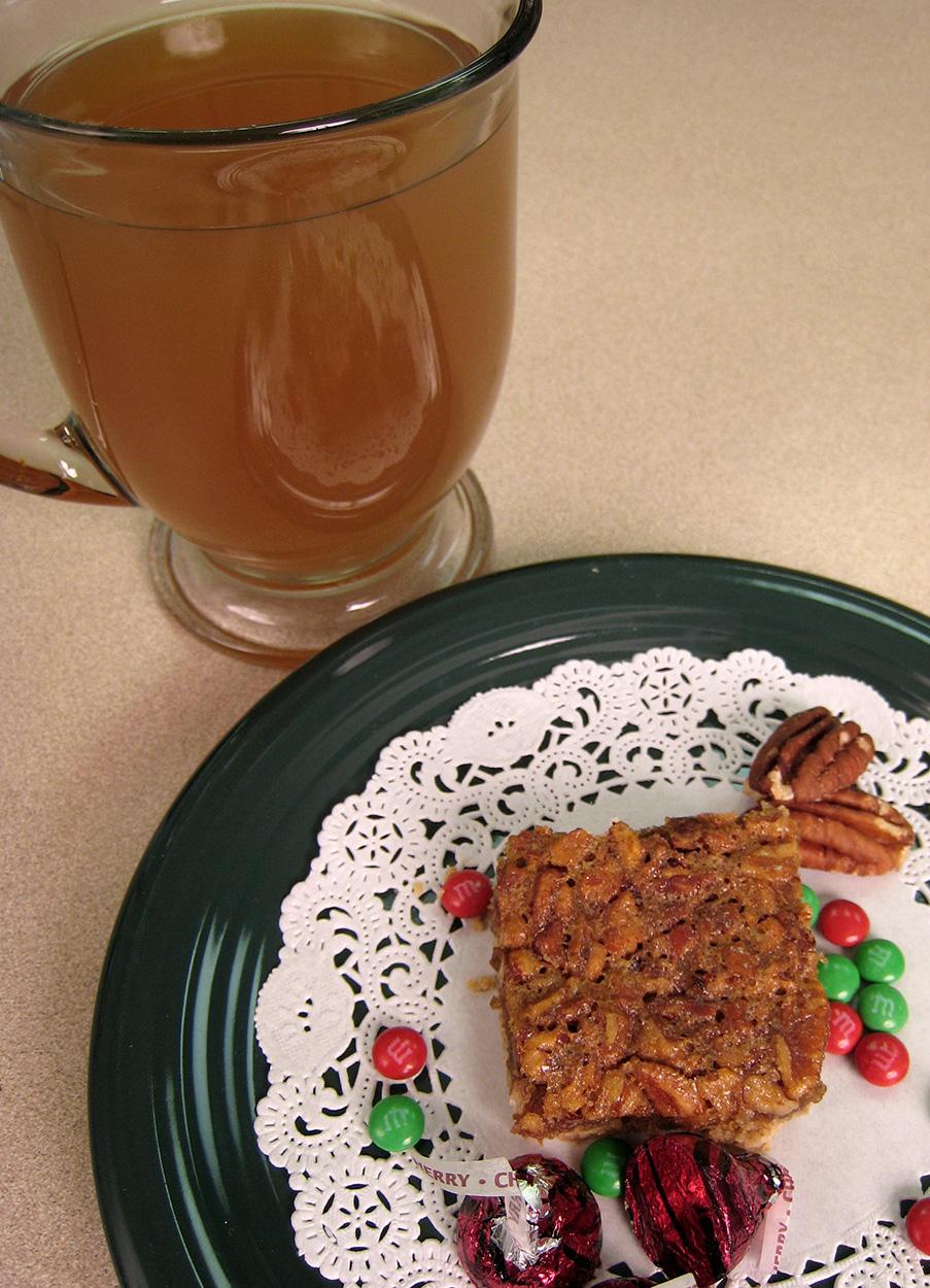 Pecan pie bar on a plate with a glass of apple cider next to it. 