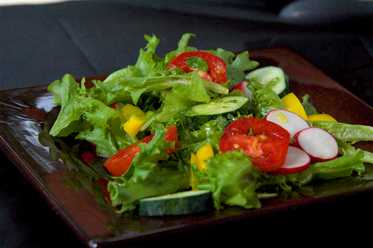A brown plate filled with a fresh green salad, tomatoes and radishes.