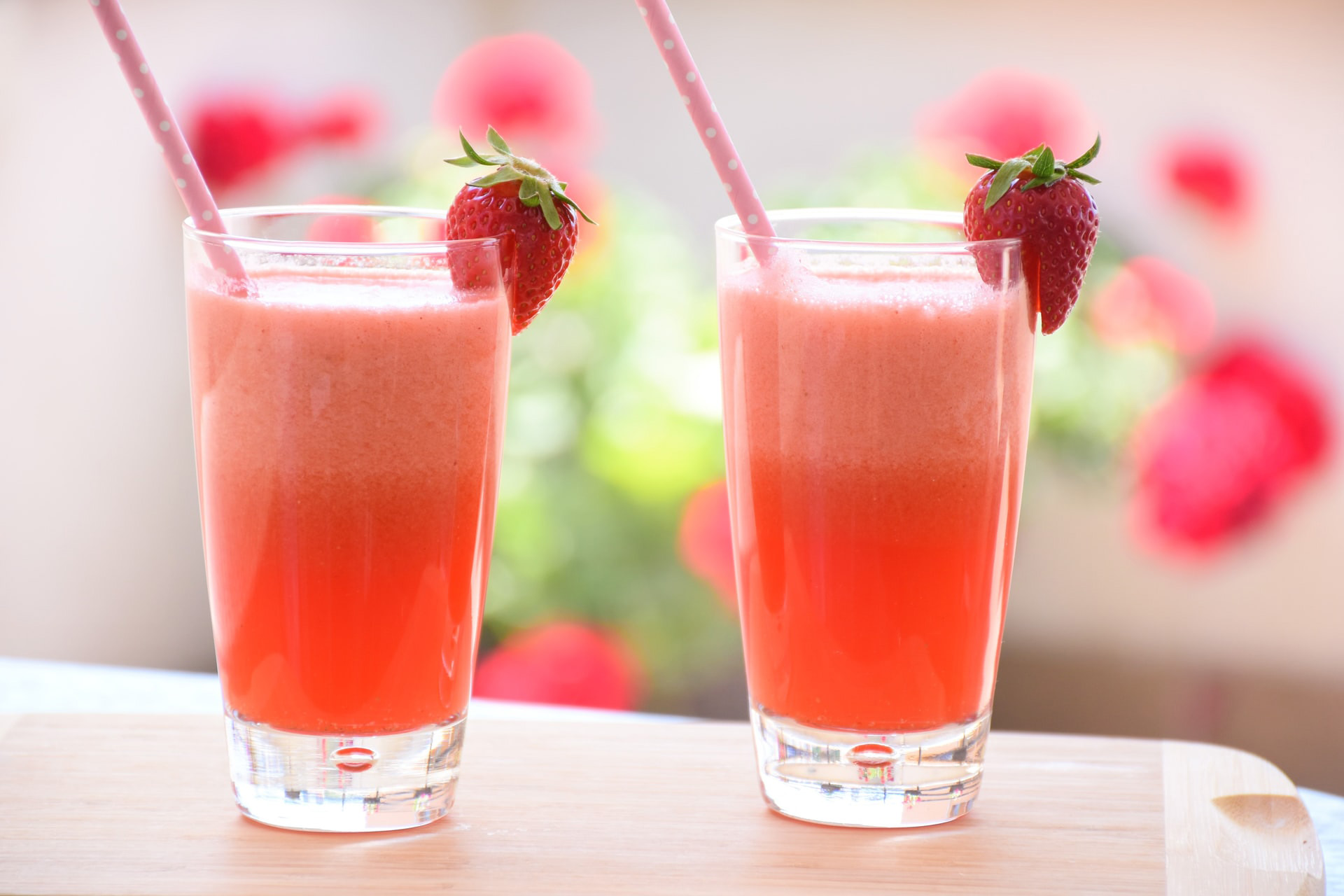 Two glasses filled with a pink liquid with a strawberry on the rim and pink polka dot straws.