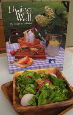 Wilted garden leaf lettuce served in a bowl in front of the Living Well book.