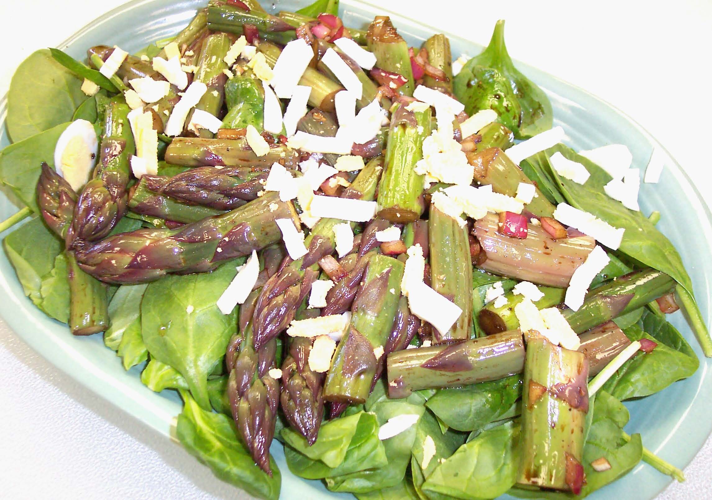 A bowl of wilted spinach and asparagus salad on a white background.