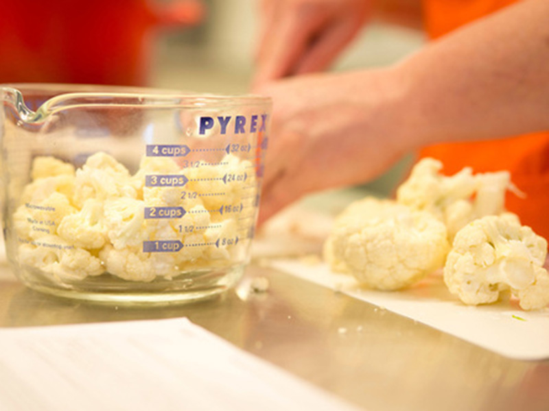 Cauliflower in a measuring cup and on a cutting board.