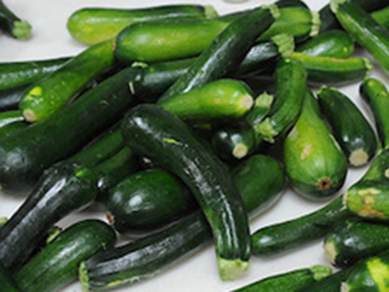 Many green zucchini laid atop each other on a table.