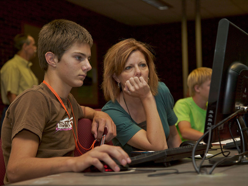 A woman helping a child on a desktop computer.