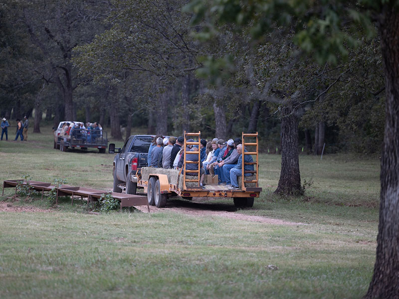 Field Day attendees sitting on hay bales in a flat bed trailer being pulled by a truck to the event location.