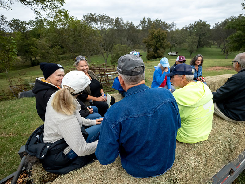 Field Day attendees talking and laughing with each other while sitting on hay bales.