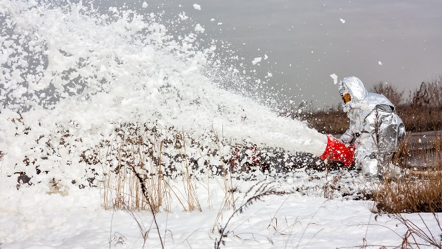 A person in a snow suit blowing snow in a field. A person in a snow suit blowing snow in a field.
