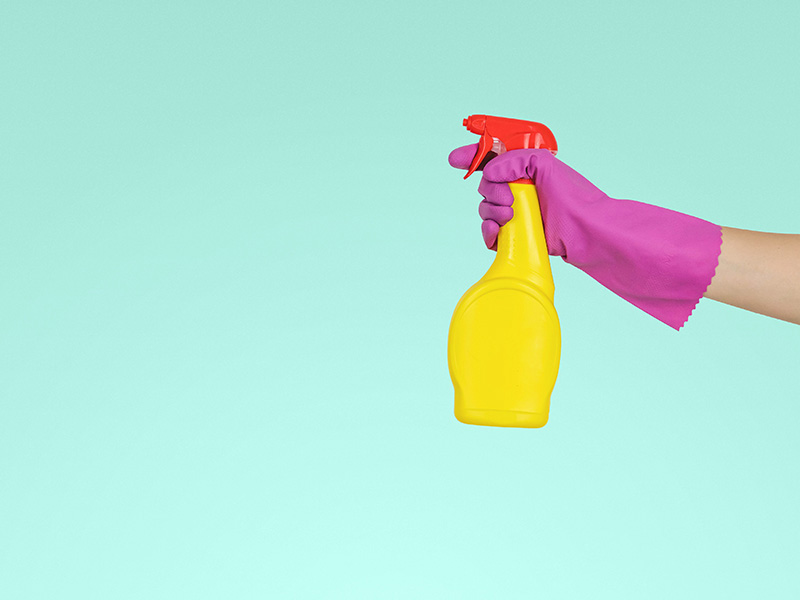 person with pink glove holds yellow spray bottle