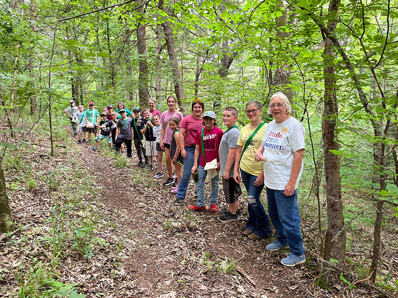 A 4-H volunteer standing in a wooded area with 4-H members.